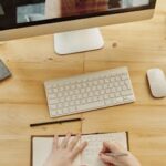 A student taking notes during an online learning session with a teacher on a monitor.