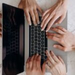 A top-down view of multiple hands typing on a laptop keyboard on a marble desk, indicating teamwork.