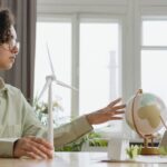 A young woman explores renewable energy with a globe and wind turbine model indoors.