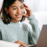 A young woman smiling as she uses a laptop in a cozy indoor setting, creating a comfortable workspace atmosphere.