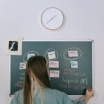 A young woman writes on a blackboard in a contemporary office setting, engaging in creative project planning.