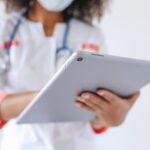 Close-up of a doctor wearing a mask using a tablet for healthcare management.