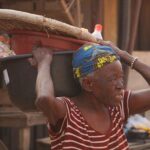 Elderly woman at an outdoor market carrying goods, showcasing small business operations.