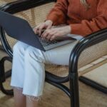 High angle of crop unrecognizable female remote employee sitting in armchair and typing on netbook while working online on startup