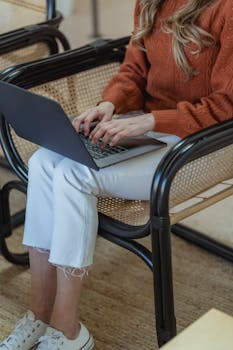 High angle of crop unrecognizable female remote employee sitting in armchair and typing on netbook while working online on startup