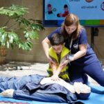 Nurse guides child in CPR training using a dummy indoors.