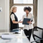 Two businesswomen discussing documents in a modern office setting.