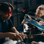 Two young engineers working on robotic equipment in a workshop setting.