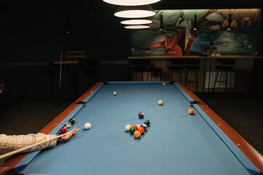 A billiard player makes a shot on a blue pool table in a dimly lit room.