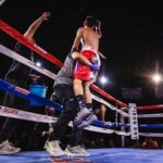 A boxer being lifted in celebration after a victory in the boxing ring, surrounded by trainers and spectators.