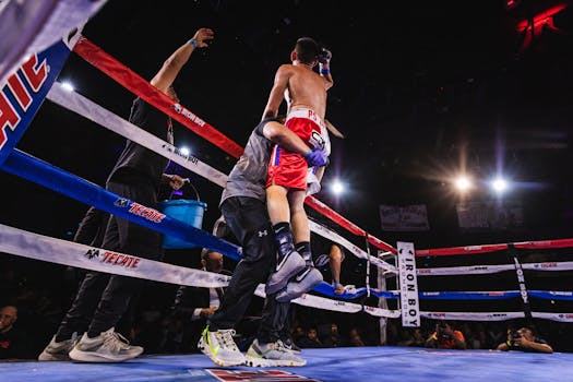 A boxer being lifted in celebration after a victory in the boxing ring, surrounded by trainers and spectators.