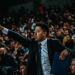 Motivated coach directing during a tense basketball game in a crowded arena.