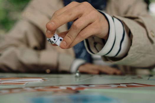 Person rolling dice during a board game, focusing on the hand and dice mid-action.