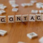 Scrabble letters spelling 'contact' on a wooden table surface.