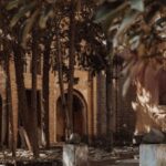 Serene courtyard with stone paths and arched building, surrounded by trees and dappled sunlight.