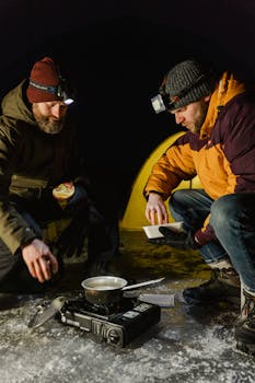 Two men cooking at a campsite on a frozen lake during a winter night.