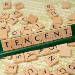 Wooden Scrabble tiles arranged to spell 'Tencent' on a green tile holder, scattered letters in the background.